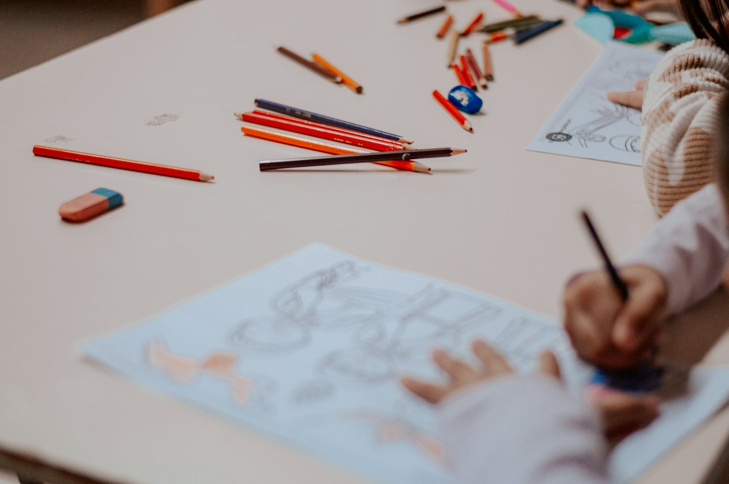 Children coloring on paper with colored pencils and an eraser.