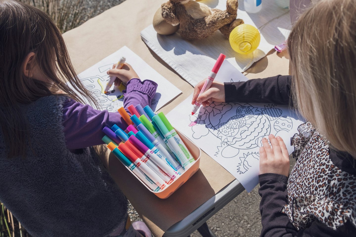 Two children coloring Easter-themed pages at a table outdoors.