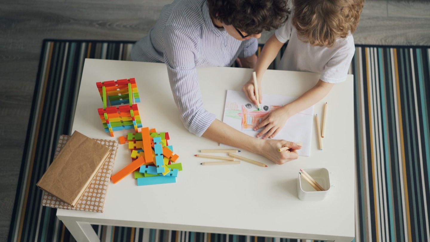 An adult and child draw together at a table.
