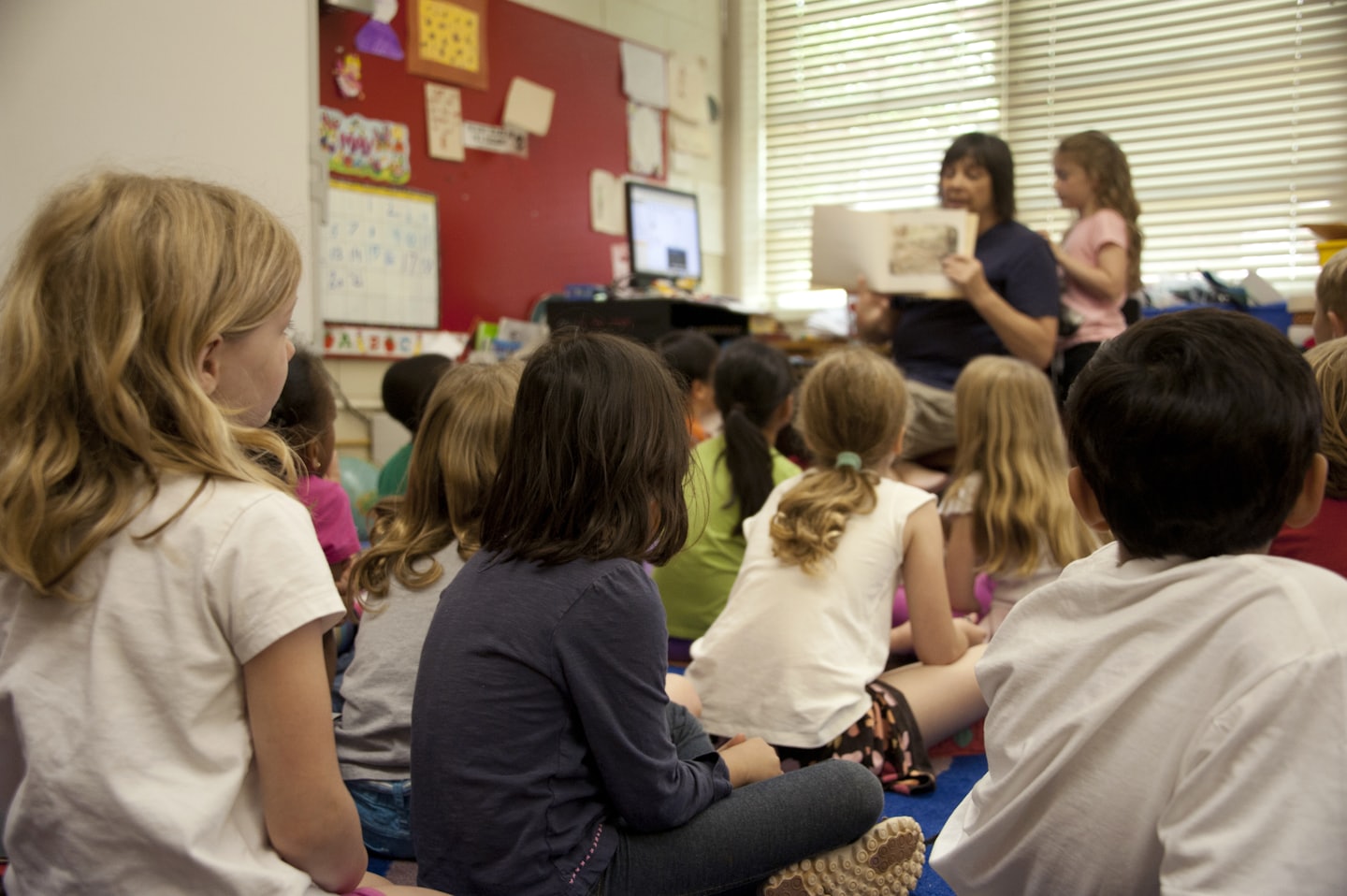Teacher reads aloud to young children sitting on a patterned carpet.