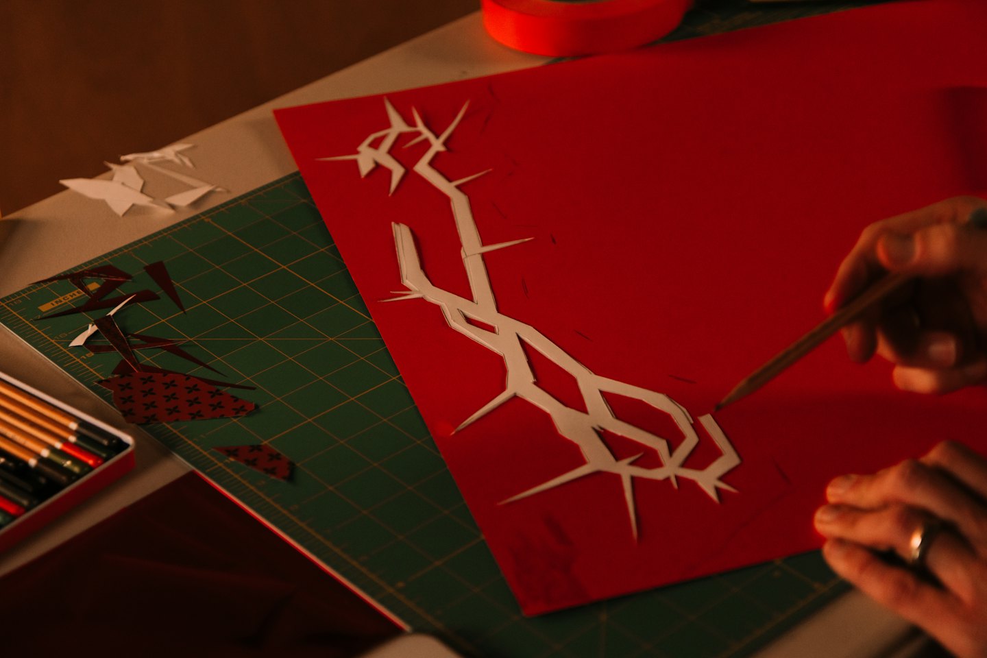 Hands carefully cutting a paper design on a green mat.