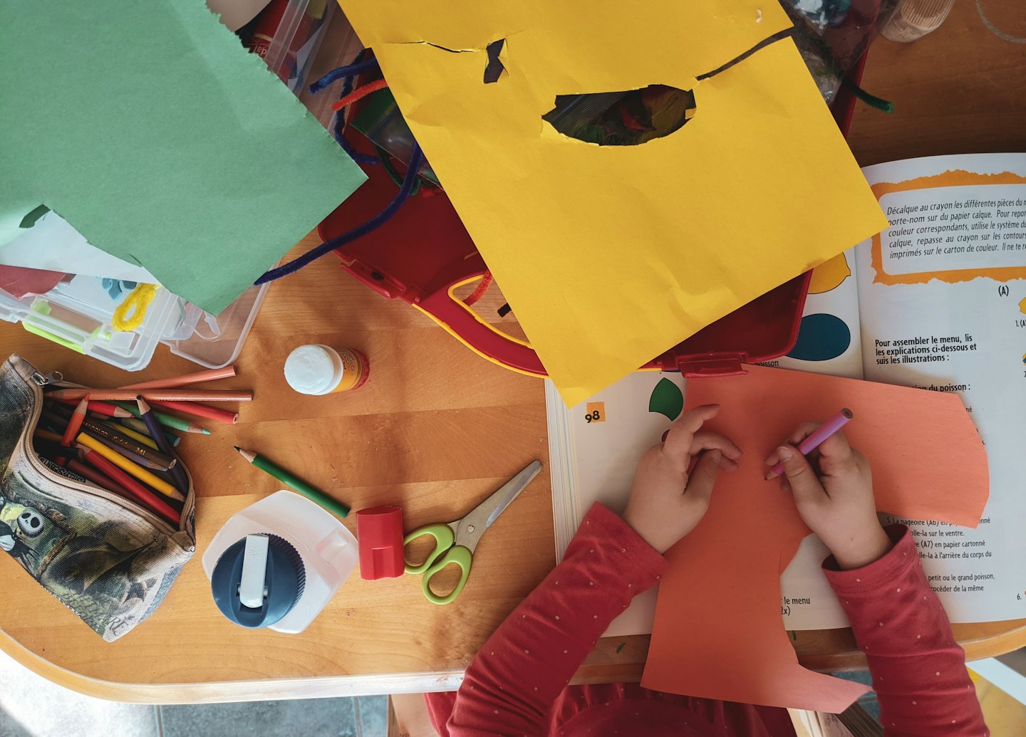 Child's hands coloring on orange paper with craft supplies.